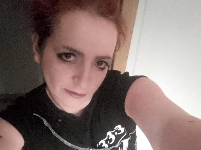 IsaWild-hot tiene el pelo rojo, piel clara y lleva una camisa negra. Está mirando hacia la cámara con una ligera sonrisa, tiene ojos marrones y un maquillaje sutil..