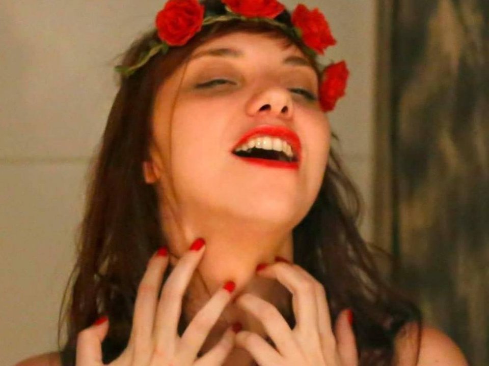 AmilyJones with long black hair, red lipstick, green bra, holding her tits, gold necklace, pink nails, bracelet, smiling, indoors. Boobs, tits, green bra, red lips, jewelry.