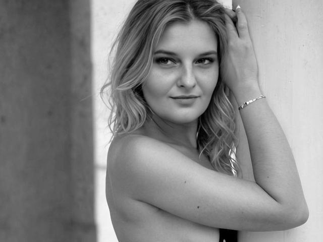 Schwarz-weißes Foto von AssiaS' Gesicht, das ihre welligen blonden Haare, die leicht gerunzelte Stirn und die konzentrierten Augen mit dunklem Eyeliner zeigt. AssiaS' Nase ist teilweise sichtbar..