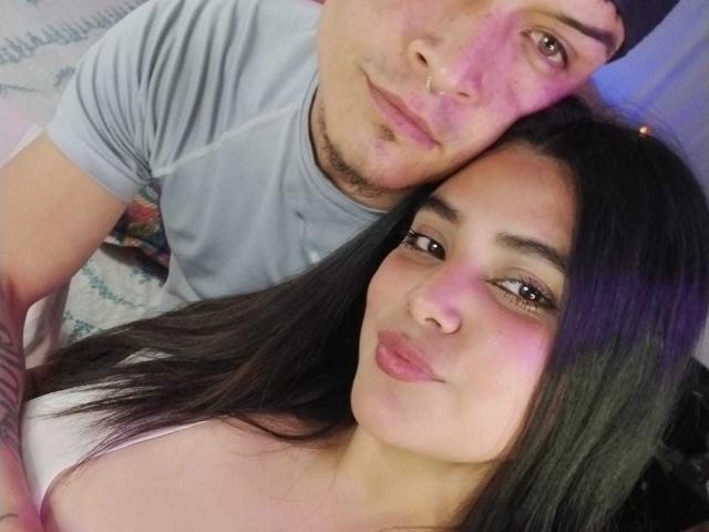 TommyAndGrace with a nose ring, wearing a gray tee, has a tattoo on his arm, leaning on dark-haired Grace who has pink lips and brown eyes.