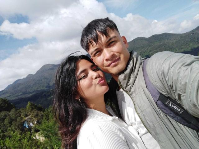 TommyAndGrace with black hair and white shirt, TommyAndGrace with short black hair and green jacket, both smiling, standing outdoors, TommyAndGrace's arm around TommyAndGrace's shoulder.