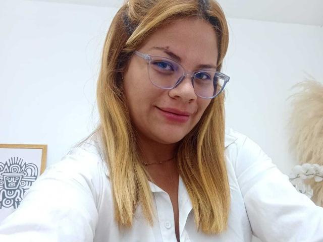 JaddeShine hat blondes Haar, klare Brillen und ein weißes Hemd, mit einem leichten Lächeln, das ihre rosafarbenen Lippen und ihre helle Haut zeigt. Ihre Brüste sind klein, und sie ist süß..