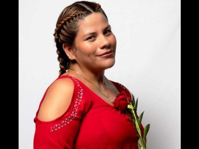 JaddeShine mit braunen Zöpfen, rotem Kleid mit Ausschnitten an den Schultern, die eine rote Rose hält, lächelnd, mittelgroße Brüste, helle Haut, Halskette, Porträt, weißer Hintergrund..