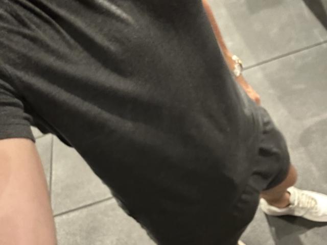 Le t-shirt noir d'OnlyRoro, qui laisse entrevoir une partie de leurs fesses, est porté avec des baskets blanches sur des carreaux gris. La main droite d'OnlyRoro est posée sur sa hanche, et elle porte une montre en or..