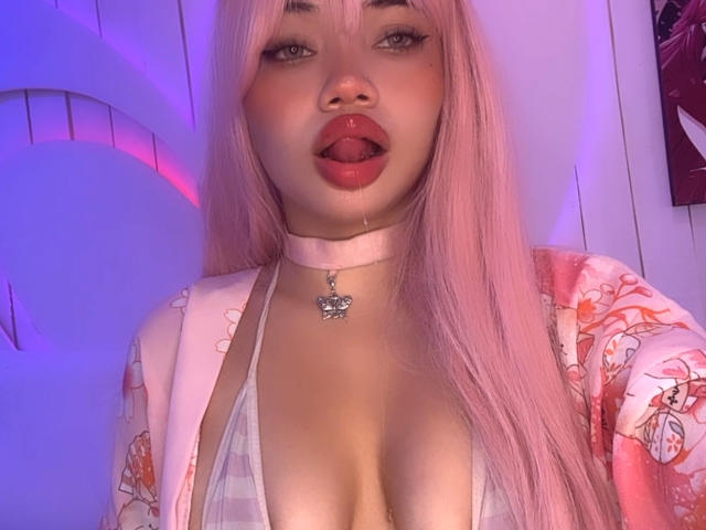 CoquineElise with red lace bra and matching panties, showing her tits and pussy, has a tattoo on her thigh, blonde hair, and sits on a pink bed.
