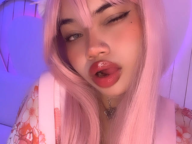 LiliMays with pink hair, floral kimono, red lips, and butterfly necklace, showing a cute, sexy face with a slight smile. Her tits are partially visible.