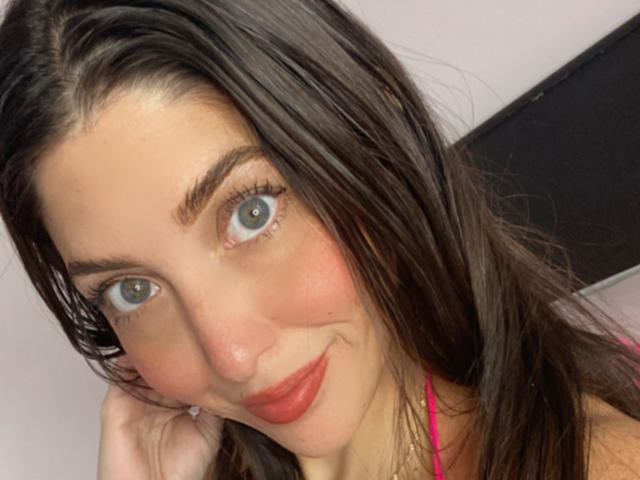 YejSusen ha gli occhi azzurri, i capelli castano scuro e un leggero sorriso con rossetto rosso. Sta toccando la guancia, indossa una maglietta rosa. Le sue natiche non sono visibili..