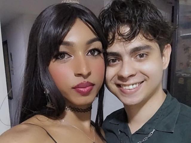MariaXJohn, avec des cheveux foncés et du rouge à lèvres rose, portant un collier, à côté de MariaXJohn, avec des cheveux noirs bouclés, une chemise verte et un sourire. Toutes les deux ont de jolis visages attrayants..