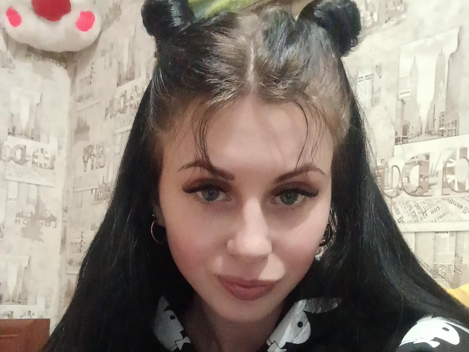 EvelynLaFire, avec des cheveux noirs et des oreilles de nounours, portant un haut noir et blanc, a les yeux bleus, un trait d'eye-liner noir, et un léger sourire, avec de petites boucles d'oreilles, sur une photo d'elle-même..