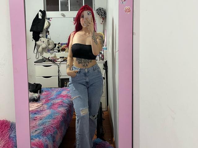 SammyViolet with red hair, black strapless top, and ripped blue jeans, standing in a mirror, showing tattoos, holding phone, hands in pockets, medium tits, cute ass.