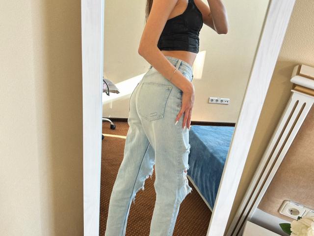 Karish's ass is in light blue, ripped jeans. She's wearing a black crop top, showing a slim, toned figure. Her long, brown hair is partially visible. Mirror selfie.