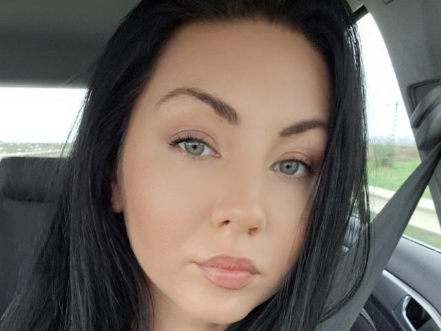 El rostro de TanyaDevon, con piel pálida, ojos verdes y cabello negro, se ve serio dentro de un coche. Su pequeña nariz y sus labios rosados están centrados en la toma..