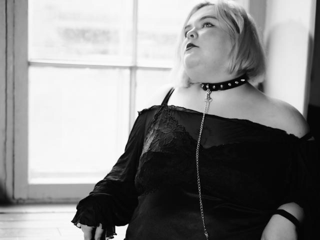 EllaBigBabe's bare butt, holding a black shoe in her right hand, with her left arm partially visible, in a black-and-white photo. Her skin is light with some freckles.