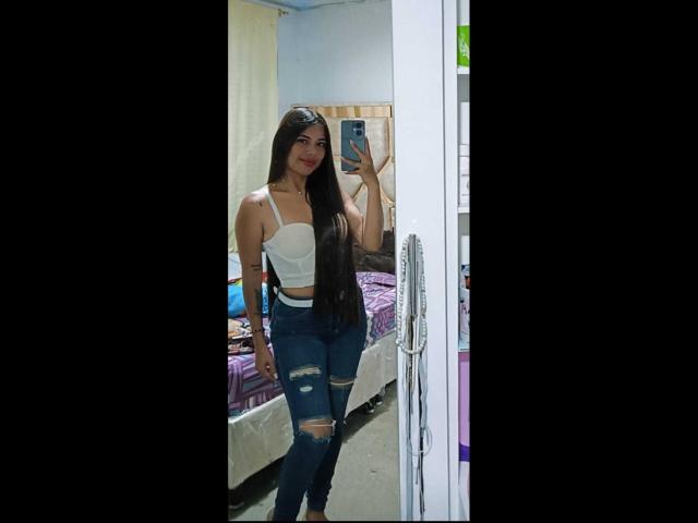 CelesteNoir, con cabello castaño largo, un top blanco sin tirantes y jeans azules rotos, sosteniendo un teléfono en un selfie frente al espejo, mostrando sus pechos y glúteos. Dormitorio, casual, sexy..