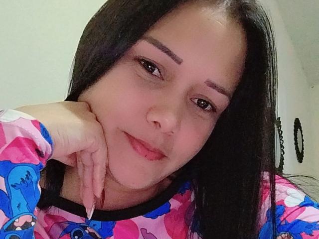 MichellSophia has long black hair, brown eyes, and is wearing a colorful shirt with blue and pink cartoon patterns. She's resting her cheek on her hand with a slight smile.