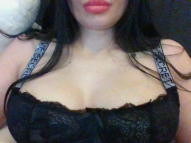 NastyaPope's tits in a black lace bra with patterned straps, showing her cleavage and pink lips. Her long black hair is down, covering parts of her face.