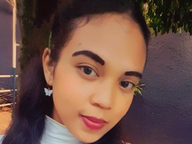 Diana69g has light brown skin, dark eyebrows, and long black hair. She's wearing pink lipstick and butterfly earrings, with a slight smile and green eyes.