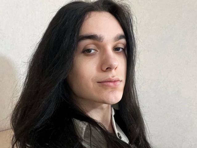 GabiYumy with long black hair, brown eyes, light skin, slight smile, wearing a grey shirt, looking off-camera. Her nose is small, and her eyebrows are thick.