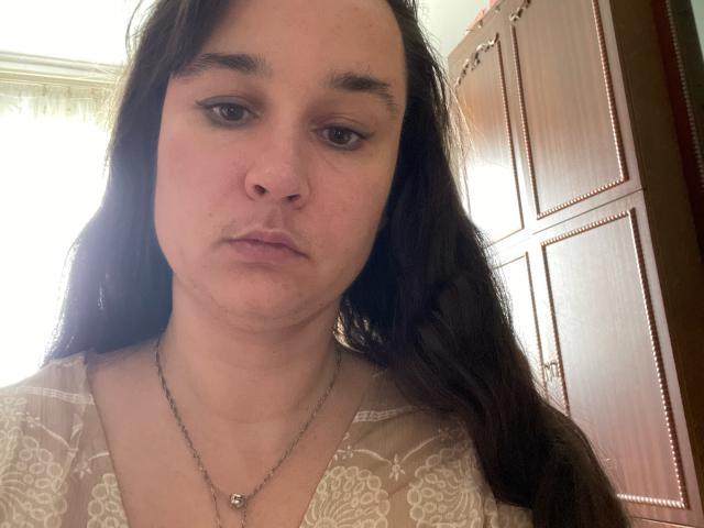SaliBerry has long dark brown hair, a serious face, and is wearing a lace-patterned top with a necklace. She has small tits and a slight nose.