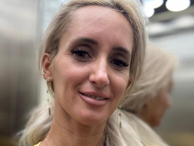 IsabelleEthan has blonde hair, small tits, and a cute smile. She's wearing a gold necklace and has long, wavy hair in a ponytail. Her reflection is in the mirror.