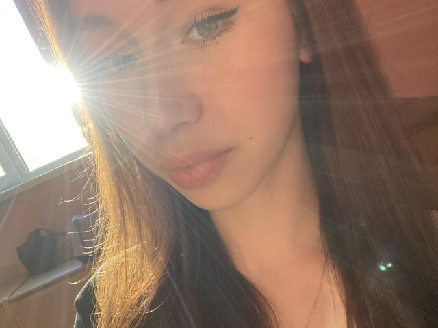 MuaShimur's face with sun flares, light brown hair, subtle makeup, and pink lips. Her eyeliner is sharp, and she has a small beauty mark on her left cheek.