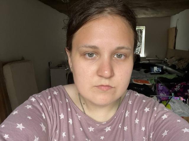 MadeleineKittie has pale skin, green eyes, and brown hair in a messy bun. She's wearing a purple star-patterned shirt, looking straight at the camera with a neutral expression.