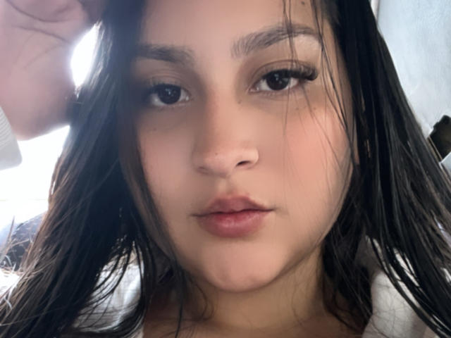 MiaCooperr a les cheveux noirs et humides, des sourcils foncés, de longs cils et une expression neutre avec des lèvres légèrement entrouvertes et rosées. Sa peau claire est visible. Elle regarde l'appareil photo..
