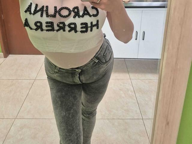 HoneyHotX mit großen Brüsten, in einem weißen Crop-Top und engen, grauen, ausgeblichenen Jeans, macht ein Selfie vor einem Spiegel und präsentiert ihren kurvigen, sexy und attraktiven Unterkörper..