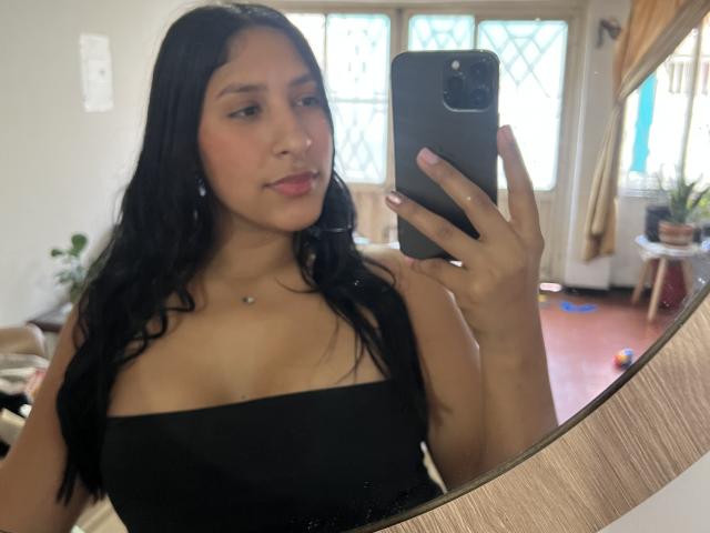 MadisonReyes with long black hair, wearing a black strapless top, taking a mirror selfie with a smartphone, showing her tits and a small necklace.