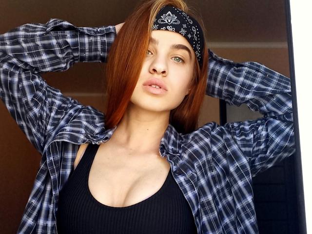 Ssimona with red hair, black bandana, plaid shirt, and black tank top, arms raised, showing small tits, pouty lips, green eyes, and fair skin.