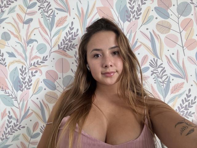 NatSorian heeft lang bruin haar, een schattige glimlach en een groot boezem, gekleed in een roze geribbelde top, en staat voor een bloemen behang. Ze heeft een tatoeage op haar rechterarm..