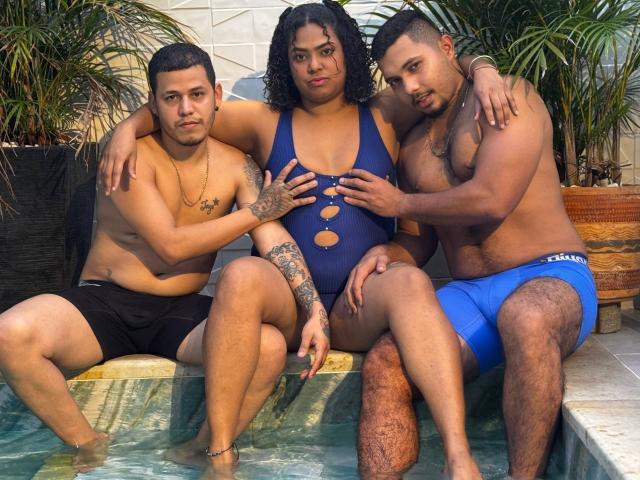 Three guys and a FantasticOrgyAD with curly hair, tan skin, and a blue cut-out swimsuit, sitting by a pool. One guy in black shorts, two in blue and black.