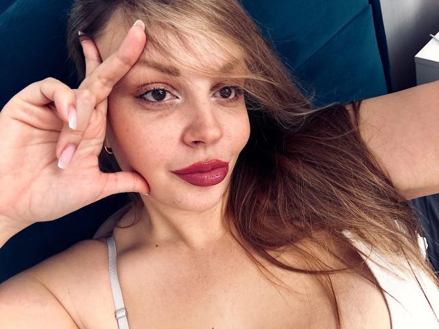 OnlyOneRose-hot with long brown hair, pink nail polish, and red lipstick, making a peace sign with her right hand, wearing a white strap, sitting in a teal car.