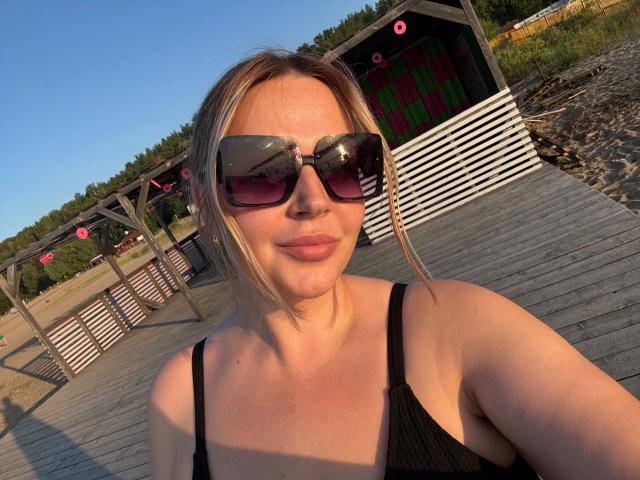 OnlyOneRose-hot with blonde hair, wearing black sunglasses and a black tank top, showing her tits, standing on a wooden dock in sunlight.