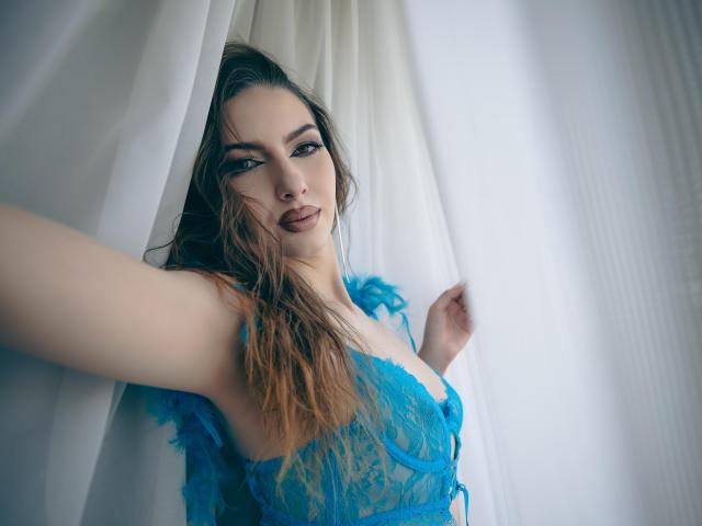 LucyGrace with long brown hair, blue lace lingerie, and parted white curtains, taking a selfie, showing her tits and slightly open mouth, looking seductive and confident.
