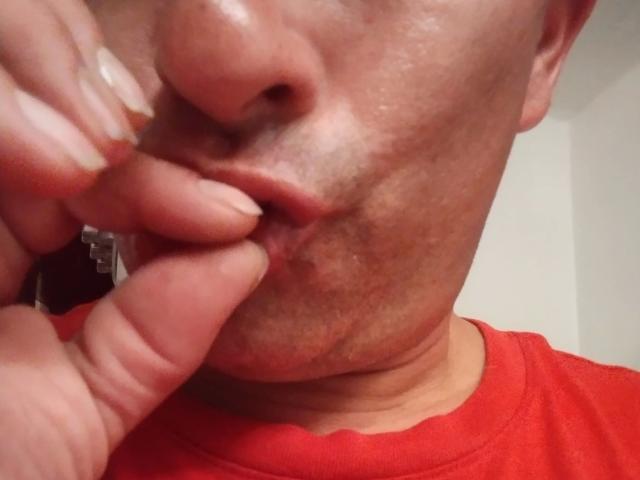 Le visage de leaveitinsideme-hot, avec les lèvres légèrement pincées, mordant un doigt dont les ongles sont sales et écaillés. Il porte une chemise rouge, et sa peau est légèrement brillante..