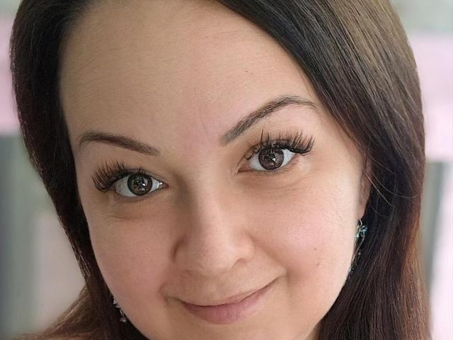 LoraHazel's face, brown eyes with long lashes, slight smile, straight brown hair, fair skin, small earrings, no makeup, soft skin texture, looking slightly to the right.