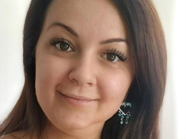 LoraHazel has brown eyes, long dark brown hair, and wears teal star earrings. She's smiling with a slight nose and small chin. Her makeup includes long, thick eyelashes.