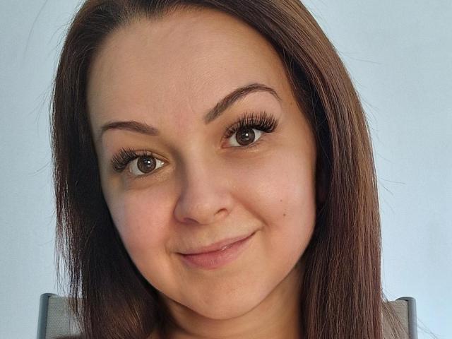 LoraHazel has brown eyes, long brown hair, and a slight smile. She's got thick eyebrows, long lashes, and a small beauty mark on her right cheek.