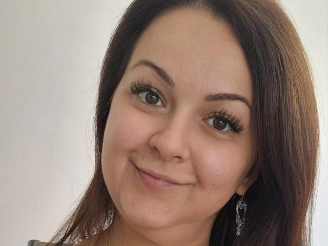 LoraHazel has brown eyes, long brown hair, and is smiling with a slight nose up. She's wearing dangling earrings and has thick black eyelashes. Her skin is light.