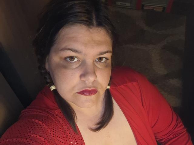 IvySexyLips with puffy face, dark brown hair in pigtails, red lipstick, red shirt, slightly sagging tits, and brown eyes, looking up with a neutral expression.