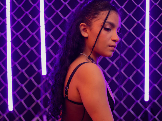 LightenStars with long curly black hair, wearing a black bra, side profile, purple neon lights, looking to the right, slim build, brown skin, subtle makeup, calm expression.