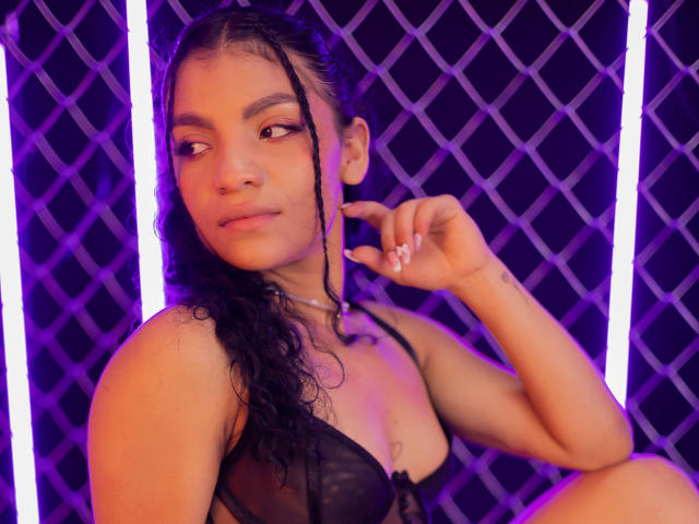 LightenStars, com cabelo preto encaracolado, pele morena e seios pequenos, vestindo lingerie de renda preta, tocando sua bochecha com um dedo, com luzes neon roxas brilhantes ao fundo..