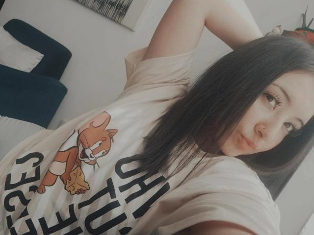 SusanMonroy with long black hair, wearing a white shirt with a cartoon mouse, looking over her shoulder, hand in her hair, soft smile, light skin, subtle makeup.