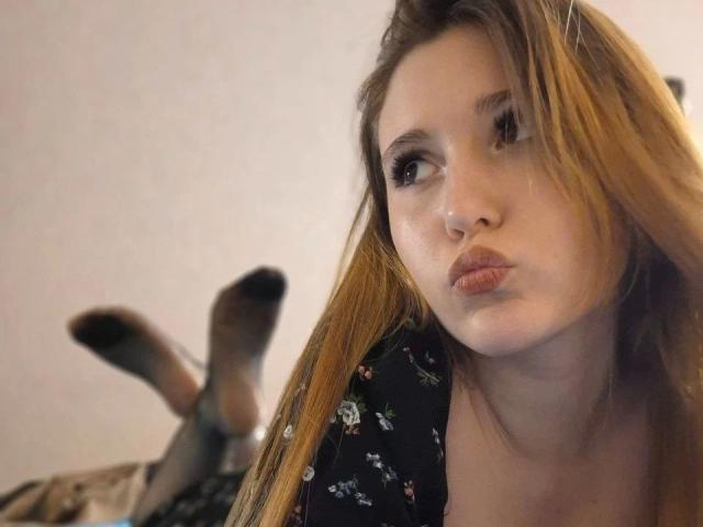 AngelinaLee-hot with pouty lips, brown hair, and a nose ring, wearing a black floral top, legs up, feet with black socks, slightly blurry, in a relaxed pose.