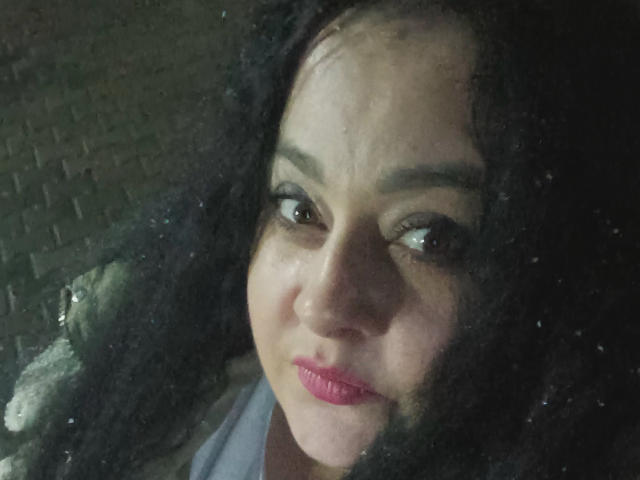 EleanorViski has dark curly hair, pink lipstick, and brown eyes, looking slightly to the side with a subtle smile. Her skin is light brown with a few visible pores.