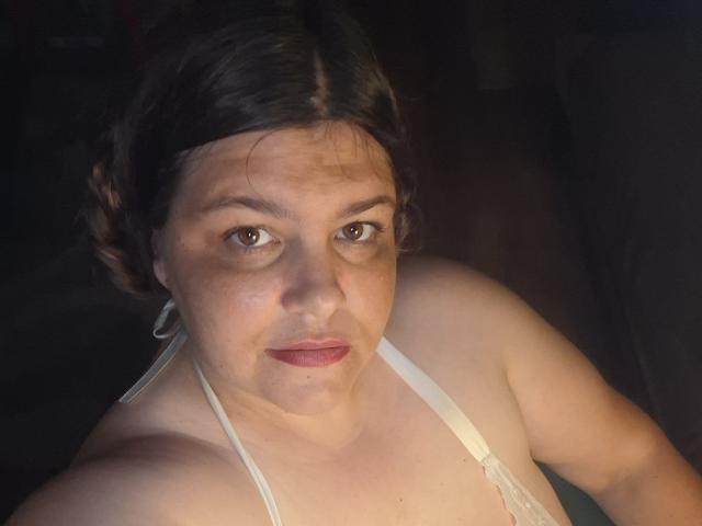 IvySexyLips has pale skin, brown eyes, and dark brown hair in a loose bun, wearing a white halter top, showing her bare shoulders and small, perky tits.