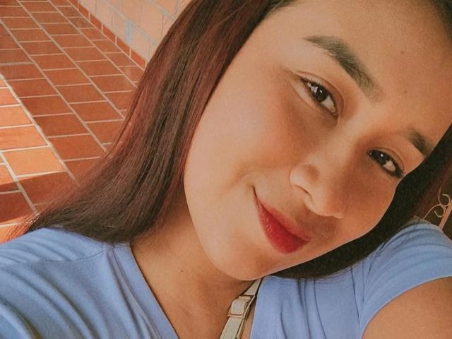 MilaWeston has a cute face with brown eyes, red lips, and straight brown hair. She's wearing a blue shirt with a white strap, smiling at the camera.