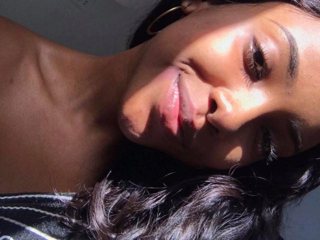 LorensX has dark brown skin, shiny black hair, and a slight smile. Sunlight casts shadows on her face. She's wearing gold hoop earrings and a black top.