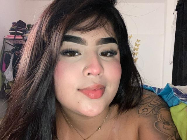 MiaHadid with dark eyebrows, long black hair, and shiny pink lips, has a nose ring, tattoo on her right shoulder, and a small amount of white fluid on her chin.